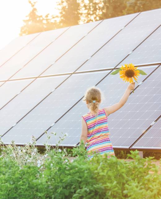 Young,6,Year,Old,Blonde,Girl,Child,Standing,In,Front Young 6 year old blonde girl child standing in front of small solar panel farm in countryside. Renewable energy concept. Sun lens flare.